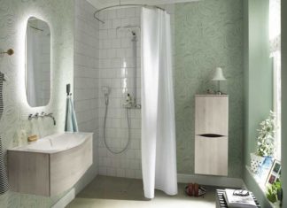 Dans une salle de bain vert céladon, une douche fermé par un rideau posé sur une tringle en arc de cercle