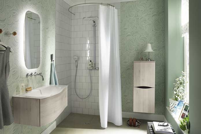 Dans une salle de bain vert celadon, une douche fermée par un rideau posée sur une tringle ronde