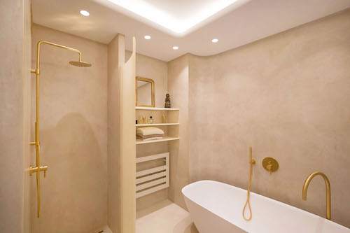 Une salle de bains en béton ciré beige et robinetterie dorée