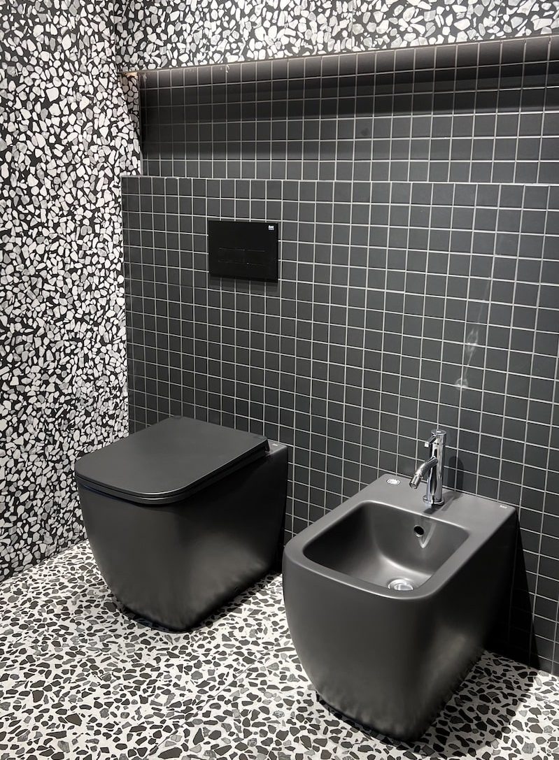 WC et bidet noirs sur un mur habillés de petits carreaux foncés
