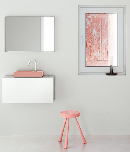 Dans une salle de bains blanche, une vasque rose sur meuble blanc avec un robinet blanc et un tabouret rose à côté.