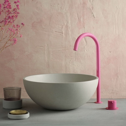 Vasque bol en béton gris clair posée devant un mur rose pastel et alimentée par une robinetterie col de cygne rose pétant 