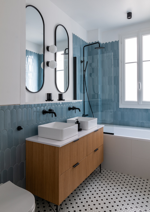 Une salle de bains avec un meuble à deux vasques en bois, un carrelage bleu au mir et des robinetteries noires.