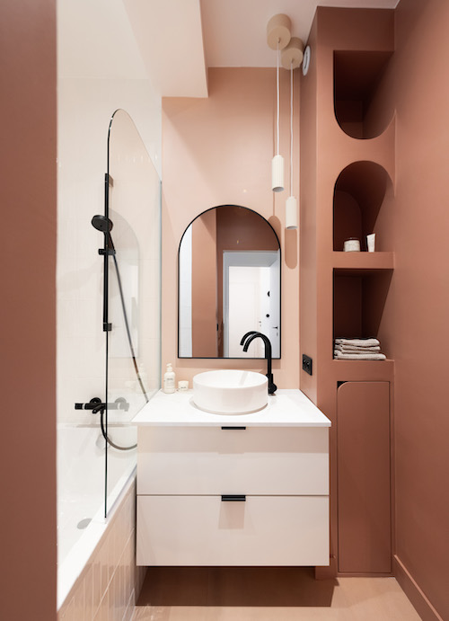 Une salle de bains aux murs blancs et terra cotta avec un meuble blanc et des robinets et accessoires noirs